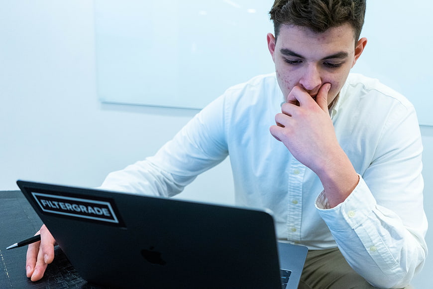 Young man thinking deeply while working on laptop in office