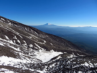 Snowy Mountain Slope with Distant Volcano Peak