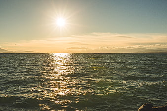 Sunset over ocean with sparkling water and distant mountains