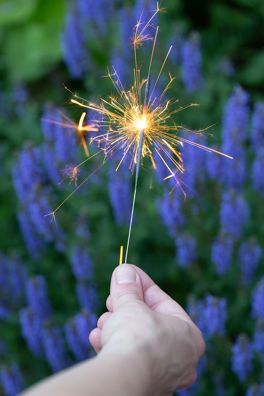 Hand holding sparkler with purple flowers background