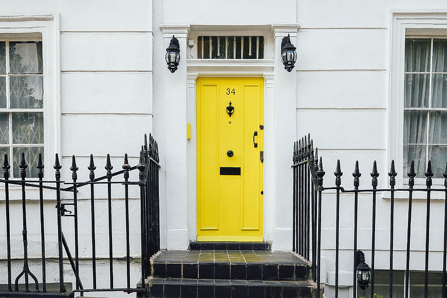 Bright yellow front door on white townhouse with black iron fence