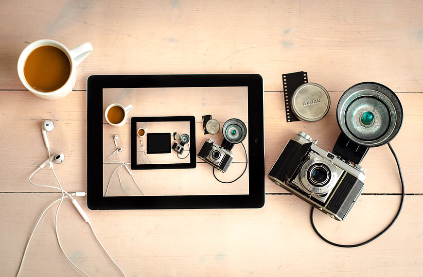 Flat lay of vintage camera, tablet, and coffee on wooden table