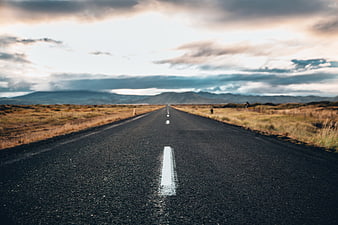 Empty asphalt road stretching to mountains under cloudy sky