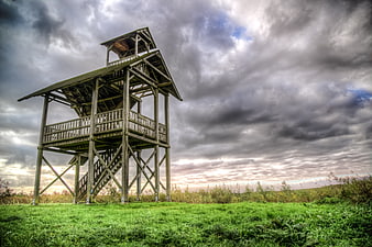 Wooden Birdwatching Tower in Green Meadow Under Dramatic Sky