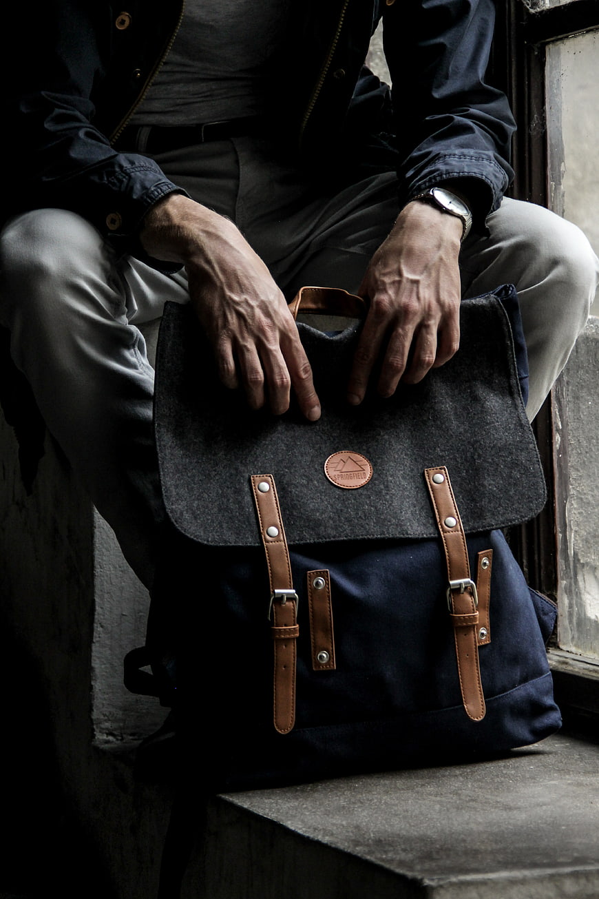 Man holding dark canvas backpack with leather straps