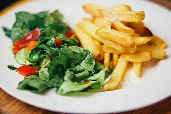 Fresh green salad and golden french fries on white plate