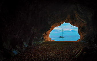 View from inside a sea cave looking out at a sailboat on the ocean