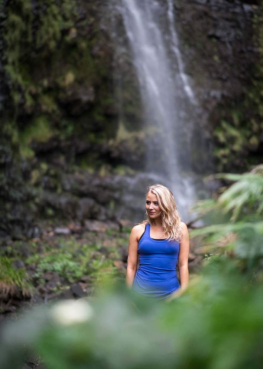 Blonde woman in blue tank top standing near waterfall