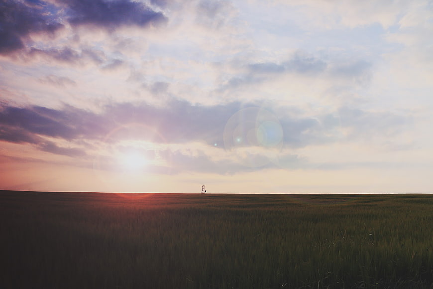 Serene Sunset Over Vast Grassland with Distant Structure