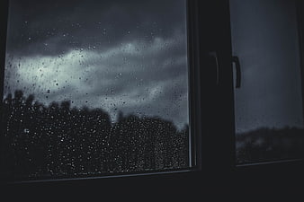 Raindrops on Window Pane Against Dark Stormy Sky