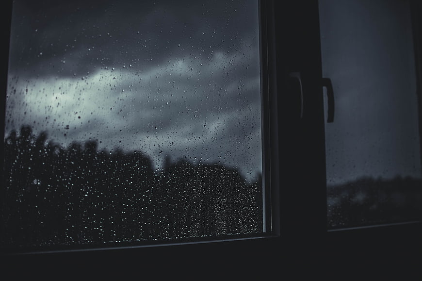 Raindrops on Window Pane Against Dark Stormy Sky
