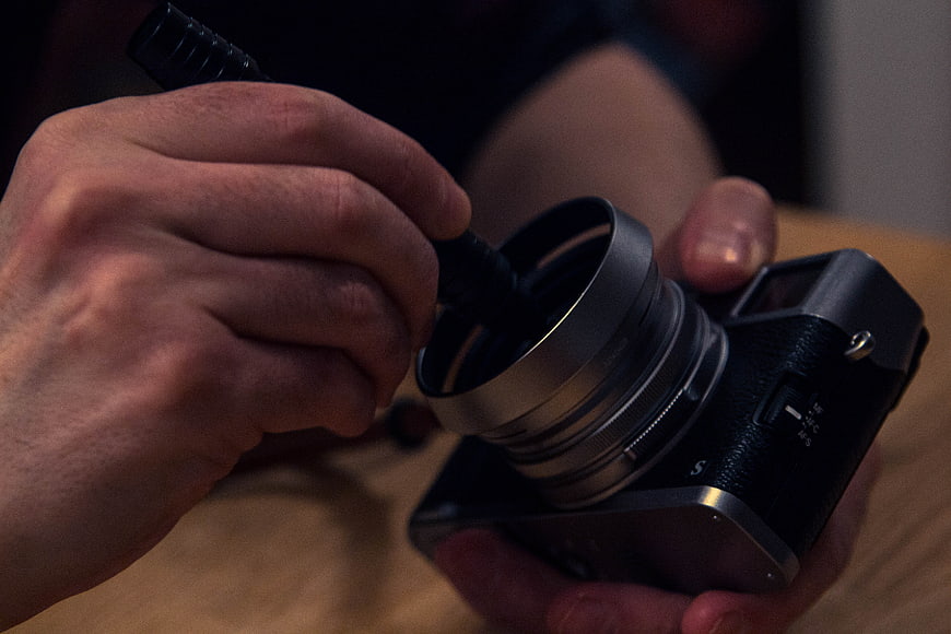 Close-up of hands cleaning camera lens with blower