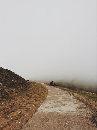 Foggy gravel road winding through misty mountain landscape