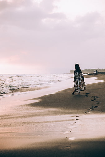Woman Walking on Sandy Beach with Footprints at Sunset
