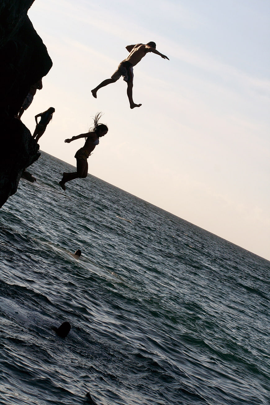 Silhouettes of people cliff jumping into the ocean