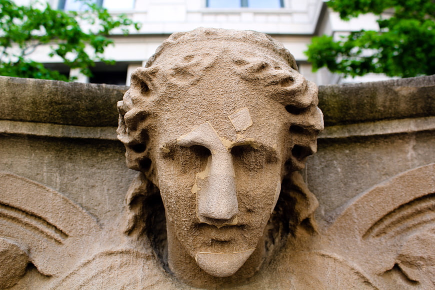 Close-up of weathered stone angel head sculpture on building facade