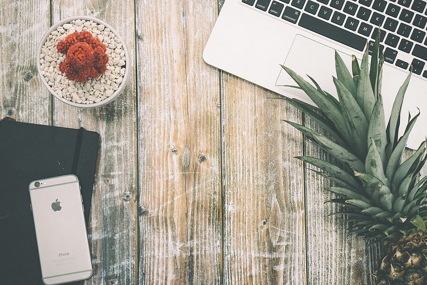 Flat lay workspace with pineapple, laptop, and smartphone on wood