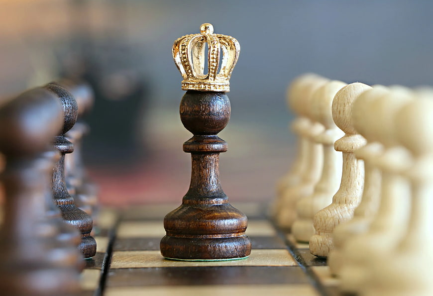 Close-up of wooden chess queen with gold crown on board