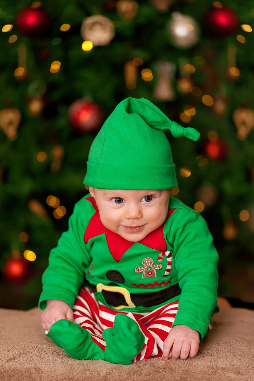 Baby in Green Elf Costume Sitting in Front of Christmas Tree