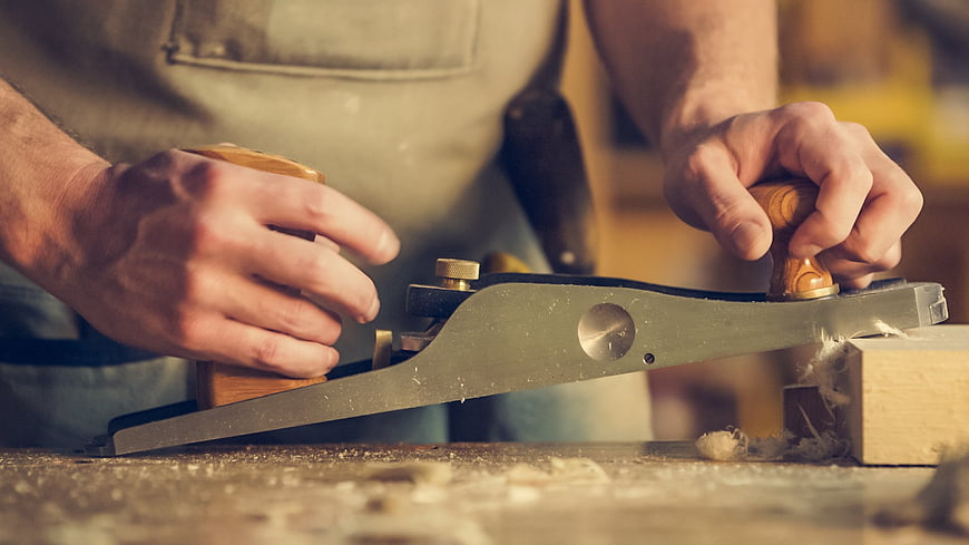 Carpenter using hand plane on wood in workshop