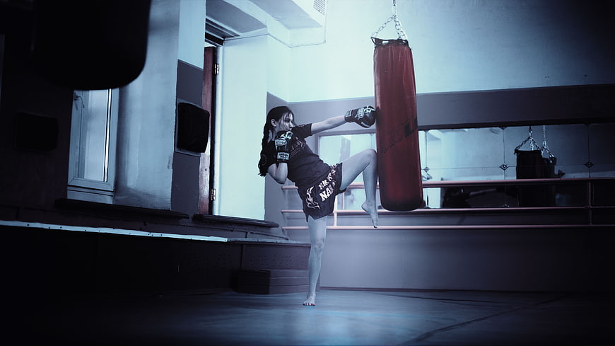 Female Muay Thai Fighter Kicking Punching Bag in Gym