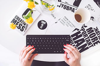 Top view of woman typing on black keyboard with coffee and flowers