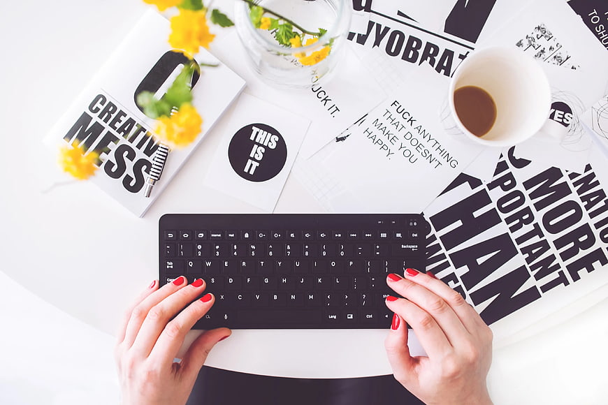 Top view of woman typing on black keyboard with coffee and flowers