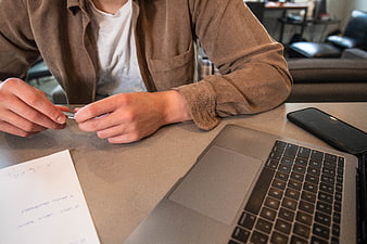Close-up of hands holding pen at desk with laptop and smartphone