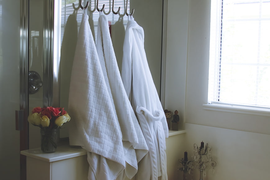 White bathrobe and towels hanging in bright bathroom interior