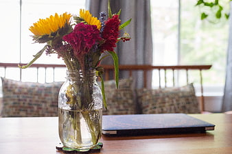 Sunflowers and red flowers in glass jar on wooden table