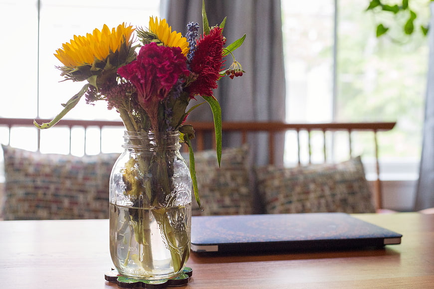 Sunflowers and red flowers in glass jar on wooden table