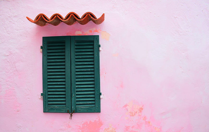 Green wooden shutters on a pink wall with terracotta roof tiles
