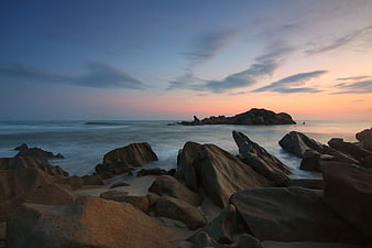 Serene Sunset Over Rocky Coastal Beach with Smooth Ocean Waves