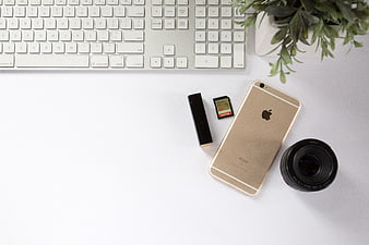 Minimalist workspace flat lay with gold smartphone, camera lens, and keyboard