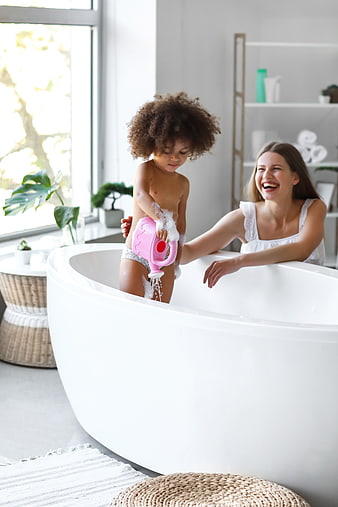 Happy mother and toddler playing with bubbles in bathtub