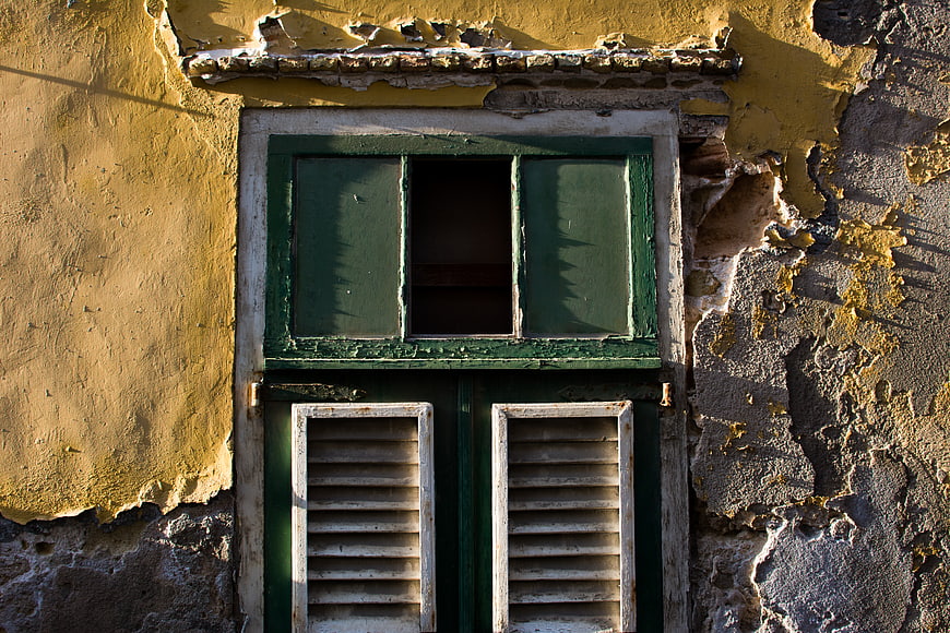 Weathered Green Wooden Window on Peeling Yellow Stucco Wall