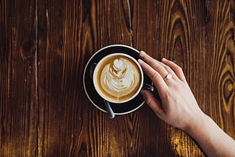 Top View of Hand Holding Latte Art Coffee on Wooden Table