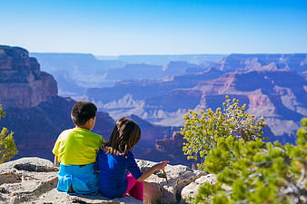 Two children sitting on a cliff edge overlooking a vast canyon