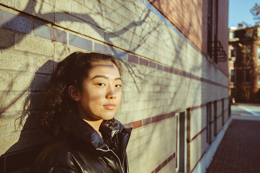 Asian woman portrait against brick wall with sunlight shadows