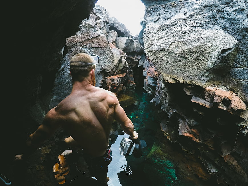 Man with underwater camera entering rocky cave pool