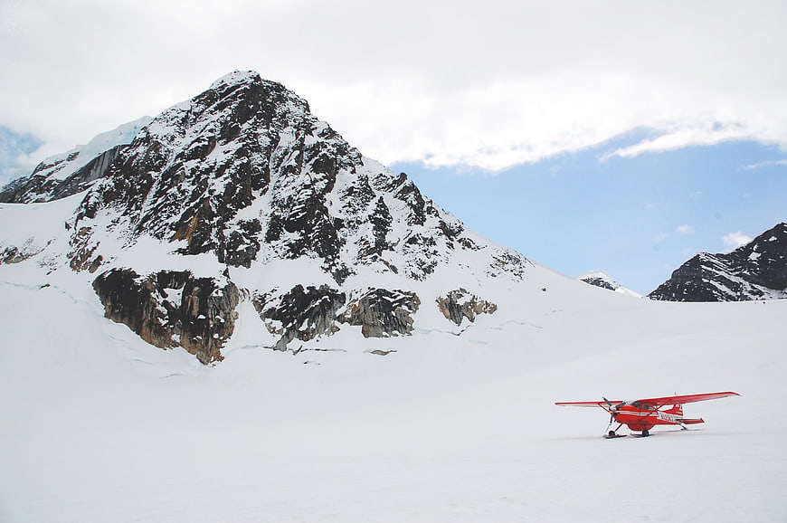 Red ski plane on snowy glacier with mountain peak