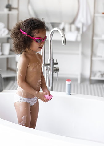 Cute child in bathtub wearing pink swimming goggles