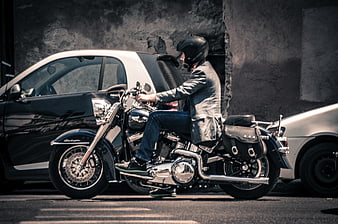 Man on black motorcycle parked between cars
