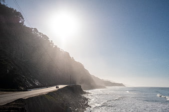 Car driving on coastal highway with sun glare and ocean view