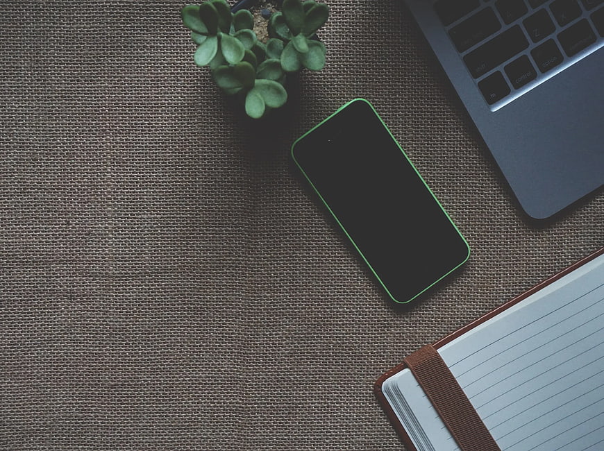 Flat lay workspace with green smartphone, laptop, and notebook