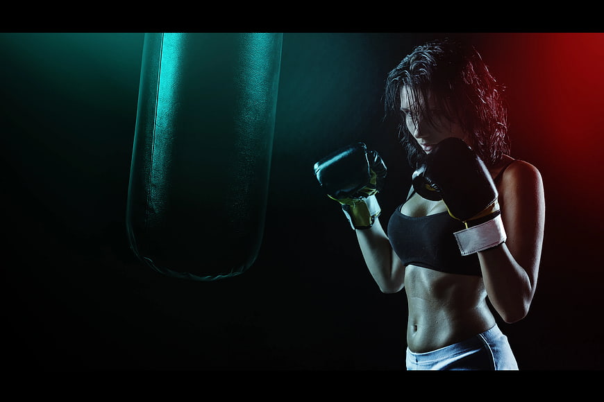 Female Boxer Training with Punching Bag in Dark Gym