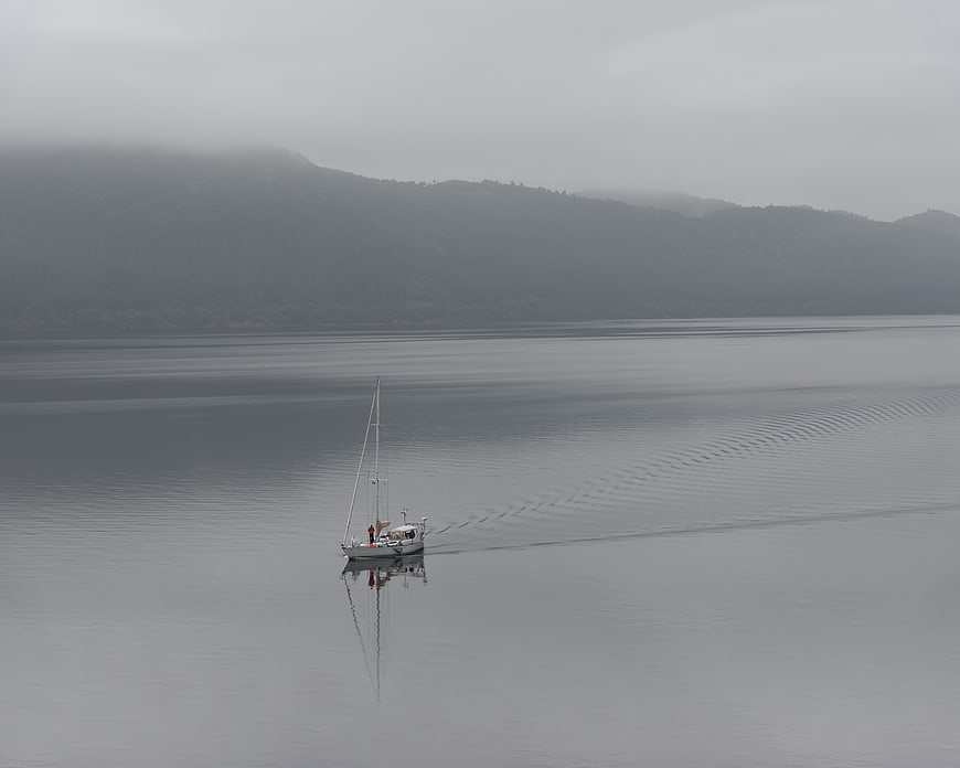 Lone sailboat on calm foggy lake with mountains