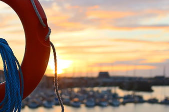 Red Lifebuoy with Blue Rope Against Sunset Marina Background