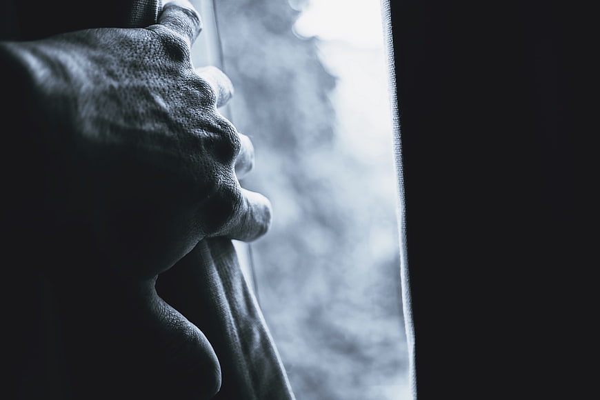 Close-up of hand holding curtain near window