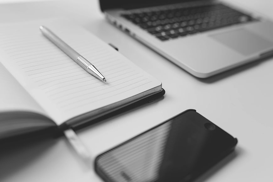 Minimalist workspace with notebook, pen, smartphone, and laptop